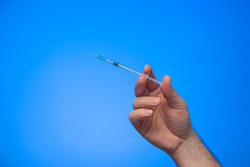 Disposable syringe with needle held in hand by Caucasian male hand studio shot isolated on blue background