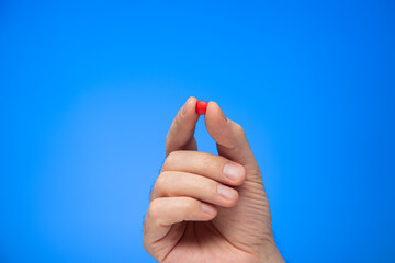 Red medical pill held between fingers by Caucasian male hand isolate on blue background studio shot
