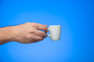Ceramic coffee cup held in hand by Caucasian male hand studio shot isolated on blue background