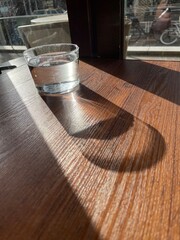 Glass of water in the afternoon sunlight on a wooden table, long shadow 