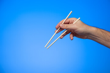Wooden Asian chop sticks held in hand by Caucasian male hand studio shot isolated on blue background