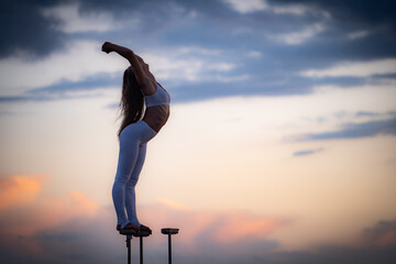 Silhouette of flexible and fit girl standing on fits with split and keeping balance against dramatic sky during sunset Concept of yoga and healthy lifestyle 