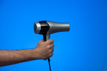 Caucasian male extended arm holding a hair dryer isolated on blue background studio shot