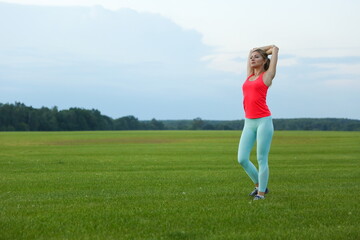 young sporty woman is doing muscle stretching and warming up outdoors in summer day