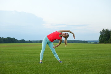 young sporty woman is doing muscle stretching and warming up outdoors in summer day