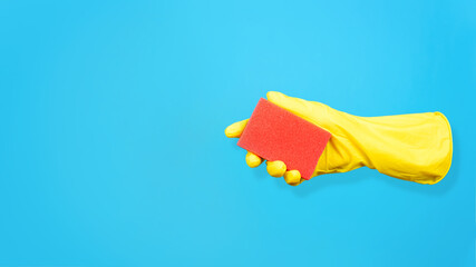 Levitating yellow glove holding cleaning sponge on blue background. Creative concept of washing and cleaning. Copy space.