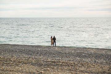 Back view of a couple hugging and watching sun on the beach. Spring or autumn.