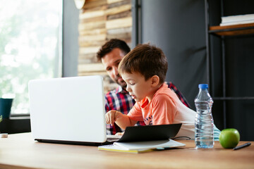 Young businessman with his son in the office. Father working on laptop while babysitting his son.