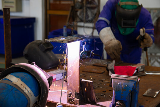 Selective focus to welding area.  Two welder are assembling the workpiece by process shielded metal arc welding. The workers are testing a welding in the workshop. - Powered by Adobe