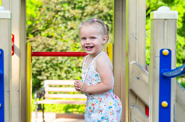 A little girl rides down a slide on a playground in the park. Holidays with children