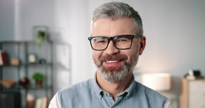 Close up portrait of happy joyful handsome middle-aged senior Caucasian man in eyeglasses looking at camera and smiling in good mood at home, positive emotions, cheerful face expression