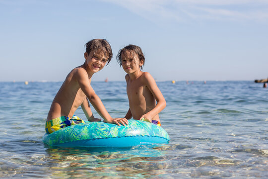 Children, preteen boys, playing on the beach with inflatable ring, having fun in the sea