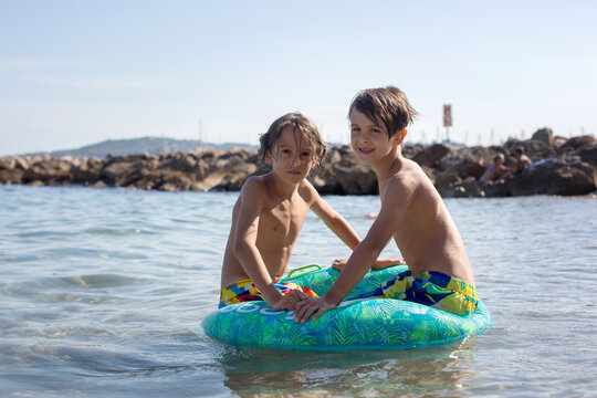 Children, preteen boys, playing on the beach with inflatable ring, having fun in the sea