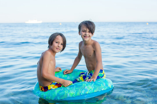 Children, preteen boys, playing on the beach with inflatable ring, having fun - Powered by Adobe