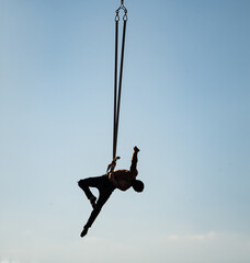 silhouette of circus artist on the aerial straps on blue sky background. Concept of art and...