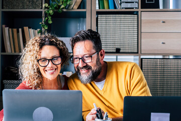 Happy adult couple work at home together with video conference call from room office in smart working and modern online digital job - young people enjoy internet connection and laptop computer