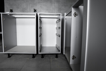 Custom kitchen cabinets installation without a furniture facades mdf. Gray modular kitchen from chipboard material on a various stages of installation in kitchen with a grey tile on floor and walls.