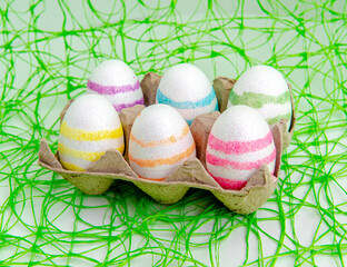 White shiny striped Easter eggs in a textured stand against a green mesh backdrop.