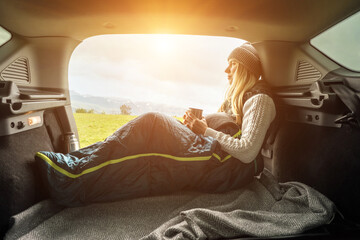 Road Trips, Girl resting in her car. Woman hiker, hiking backpacker traveler camper in sleeping bag, drinking hot tea and relaxing on top of mountain. Health care, authenticity, sense of balance