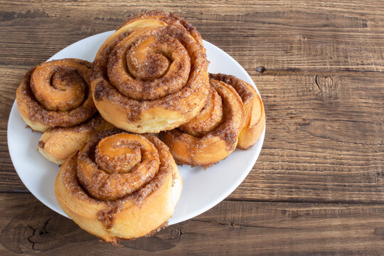 Cinnabon buns with sugar and cinnamon on a white plate on wooden background