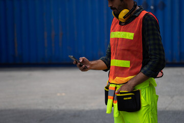 Fototapeta premium Caucasian worker in safety vest reflective with Safety helmet Typing a message on a cell phone in container pepot
