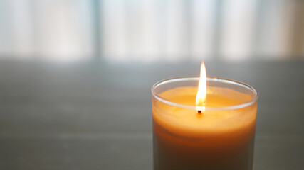 Fototapeta na wymiar close view of lit candle with a textured white and gray blurred background 