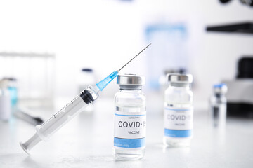 Vials with vaccine against Covid-19 and syringe on white table indoors