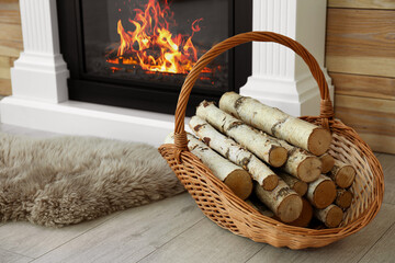 Firewood in wicker basket near burning fireplace indoors