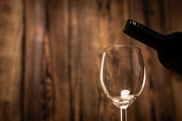 Pouring red wine into the glass against wooden blurred background.
