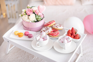 Flowers and sweets on white table and balloons on the white bed. Gift for Valentine's day or March 8 or Mother's Day or birthday