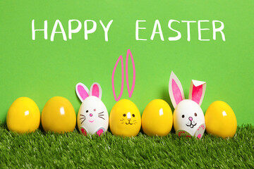 White eggs with drawn faces and ears as Easter bunnies among others on green grass