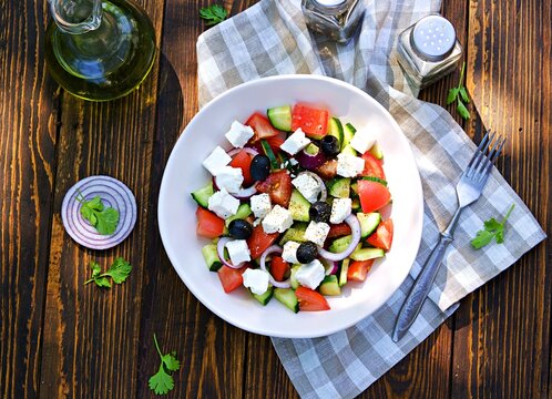 Vegetable salad with feta cheese and olives in a light ceramic bowl on a wooden background. Salad recipes.