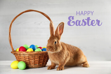 Happy Easter! Cute bunny and wicker basket with dyed eggs on white table