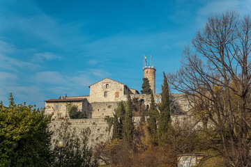 Fototapeta na wymiar Part of the castle of the city of Brescia on a sunny winter day. A view from the park. Castello di Brescia, Lombardy, Italy. Medieval castle with battlements, a tower, drawbridge and ramparts. 