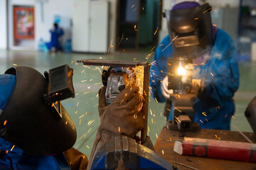 workers cutting metal sheets with electric grinder in the workshop. Welder is wear personal protective equipment(PPE) while working. Leather gloves and face shield.