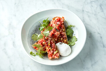Delicious tuna tartare with avocado, cilantro, served on rye croutons in a white plate with poached egg. Snack of Japanese cuisine