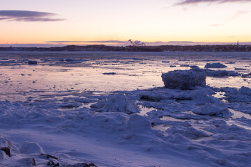 Chunks of ice on the St. Lawrence River with churches and smoking chimneys on the south coast in soft focus background seen during a blue hour morning, Quebec City, Quebec, Canada