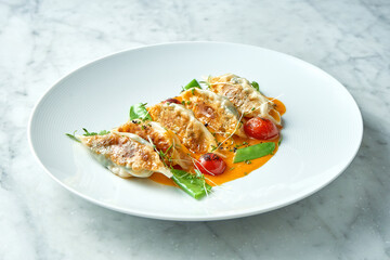 Fried dumplings or Japanese Gyoza in yellow sauce, cherry tomatoes and green peas, served in a white plate on a marble background. Pan-Asian cuisine. Restaurant food
