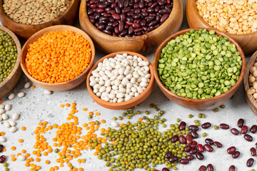 Different legumes. Mung beans, red and white beans, lentils, peas and chickpeas in wooden bowls on the light grey kitchen table. Beans closeup. Vegetarian food	