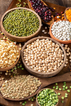 Different legumes. Mung beans, red beans, lentils, peas and chickpeas in wooden bowls on a brown wooden kitchen table. Beans close-up. Vegetarian food