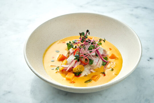 Peruvian cuisine dish - seabass ceviche with hot peppers, onions and yellow sauce, served in a white plate on a marble background. Restaurant seafood.