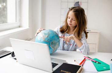 beautiful, young, blond girl is sitting in front of laptop holding globe in her hands and dreaming about vacation and end of pandemic and covid 19