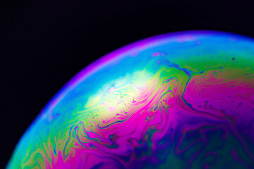 Rainbow soap bubble on a black background. Close-up of a colorful surface.
