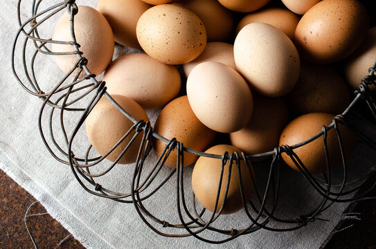 Eggs in a wired basket on a beige napkin and dark background. 