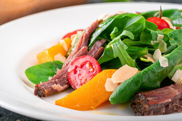 Baked pumpkin salad, spinach, tomato, almond and beef in a white plate on a stone background, close up