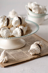 White meringue cookies with dulce de leche on a cake stand and in white and green tea cups on an old magazine, and white backdrop. 