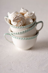 Meringue cookies in white and green tea cups on white backdrop. 