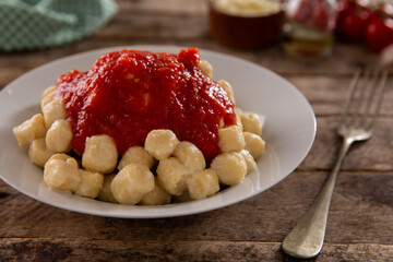 gnocchi with marinara sauce and grated cheese on a white plate and rustic wood