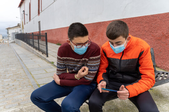 Stock photo of teenagers wearing face mask due to covid19 sitting in a bench and using phone.