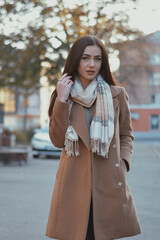 A brunette with long hair in a brown coat walks in the city center. 